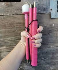 Imagem mostra uma mão branca com unhas pintadas de cor de rosa segurando uma bengala longa cor de rosa.