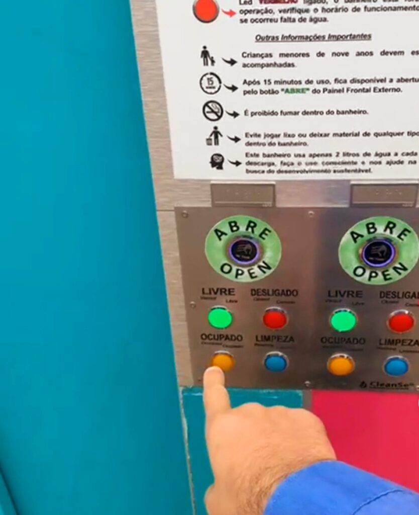 A imagem mostra uma mão apertando um botão que está em um painel com vários botões e algumas informações em tinta.