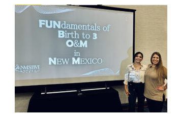 A foto mostra 02 mulheres ao lado de uma tela de projeção onde se lê "Fundamentals of birth to 3 O&M New Mexico"